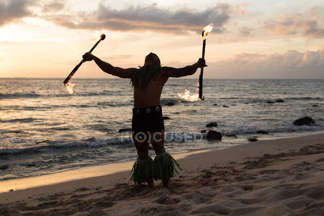 Homme danseur de feu performant avec des bâtons de levi de feu à la plage au crépuscule — Photo de stock