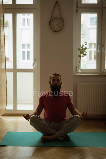 Человек, выполняющий йогу на коврике для упражнений дома — стоковое фото