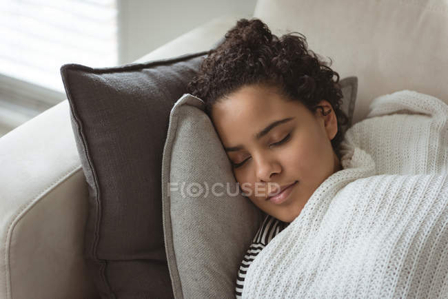 Mulher envolta em cobertor dormindo no sofá em casa — Fotografia de Stock