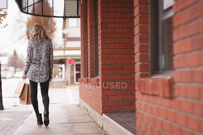 Vista trasera de la chica con bolsa de compras caminando en el pasillo fuera del centro comercial - foto de stock