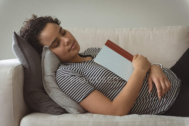 Femme dormant tout en tenant le livre dans la main sur le canapé — Photo de stock