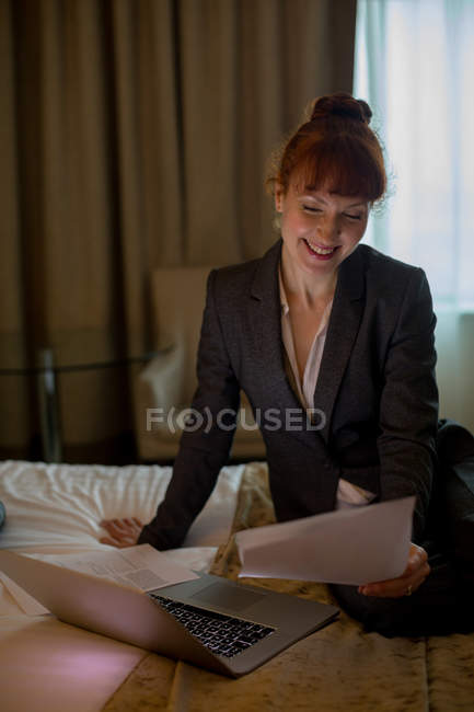 Geschäftsfrau betrachtet Dokumente auf einem Bett im Hotelzimmer — Stockfoto