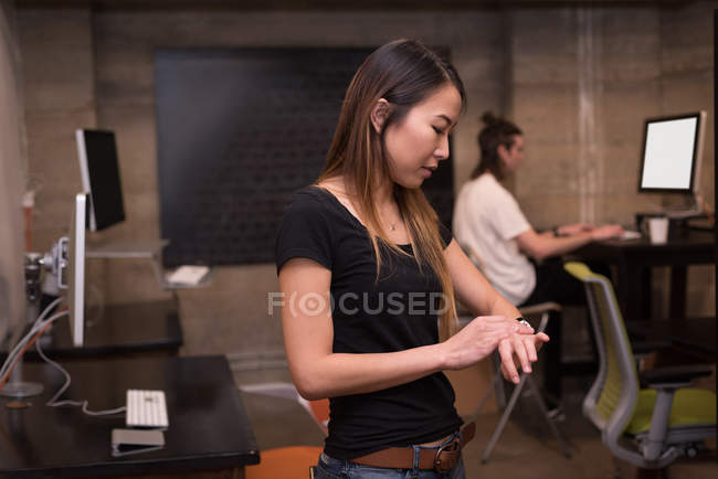 Жіночий виконавчий за допомогою smartwatch в офісних оформлення інтер'єру. — стокове фото