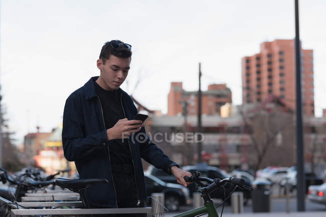 Homem de pé ao lado de sua bicicleta e usando telefone celular na rua — Fotografia de Stock