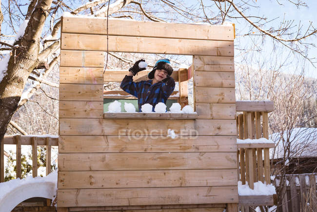 Милий хлопчик грає зі сніжним м'ячем на ігровому майданчику взимку — стокове фото