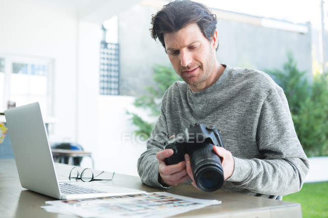 Mann benutzt Laptop und hält Digitalkamera zu Hause — Stockfoto
