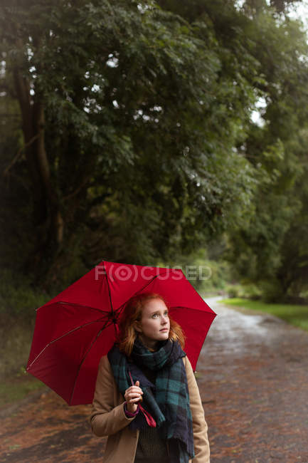 Молодая женщина, стоящая с зонтиком в парке — стоковое фото