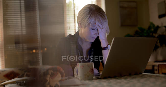 Preoccupato donna matura utilizzando il computer portatile in soggiorno a casa — Foto stock