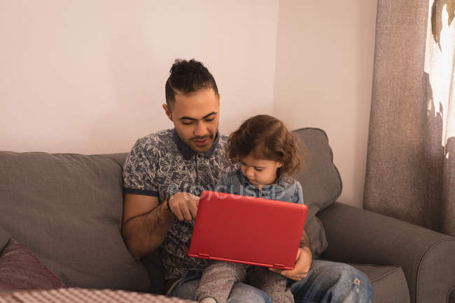 Padre e hija usando el ordenador portátil en la sala de estar en casa . - foto de stock