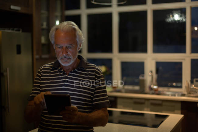 Пенсионер пользуется цифровым планшетом на кухне дома — стоковое фото