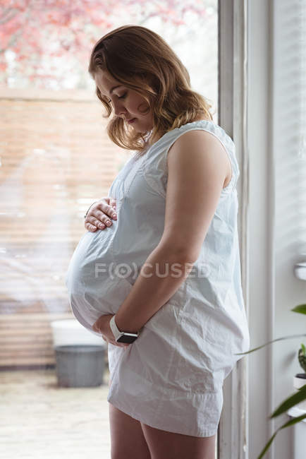 Mujer embarazada mirando hacia abajo hacia su vientre y sosteniéndolo - foto de stock