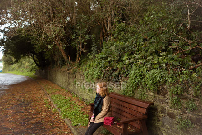 Mujer pensativa sentada en el banco en el parque - foto de stock