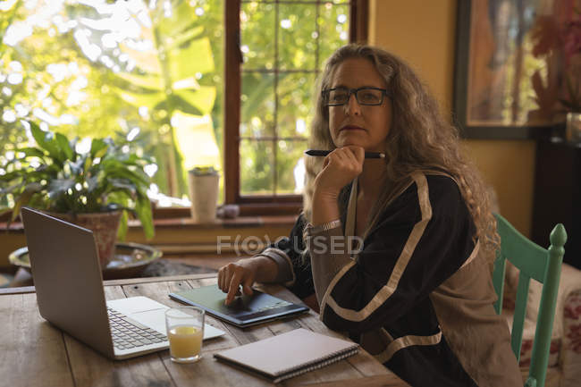 Reife Frau schaut weg, während sie zu Hause am Tablet arbeitet — Stockfoto