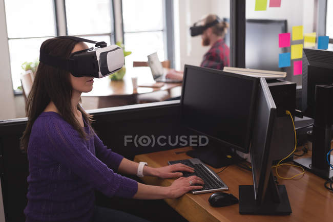 Female executive using virtual reality headset with computer at desk in office — Stock Photo