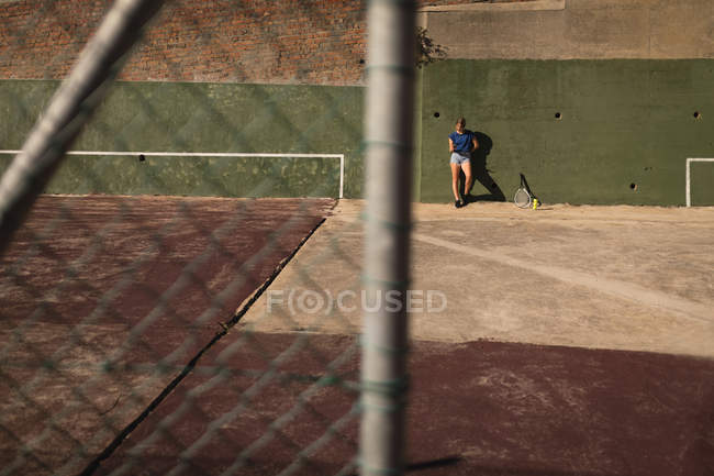 Frau lehnt an sonnigem Tag auf dem Tennisplatz an Wand — Stockfoto
