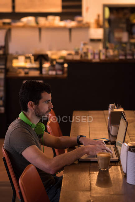 Homme adulte moyen utilisant un ordinateur portable dans un café, vue latérale . — Photo de stock