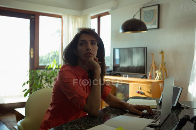 Повзрослевшая женщина смотрит в сторону, пользуясь ноутбуком дома — стоковое фото
