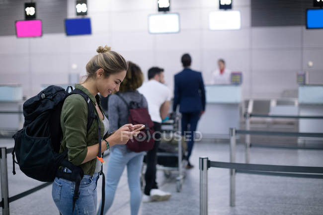 Жінка за допомогою мобільного телефону, стоячи в черзі в аеропорту — стокове фото