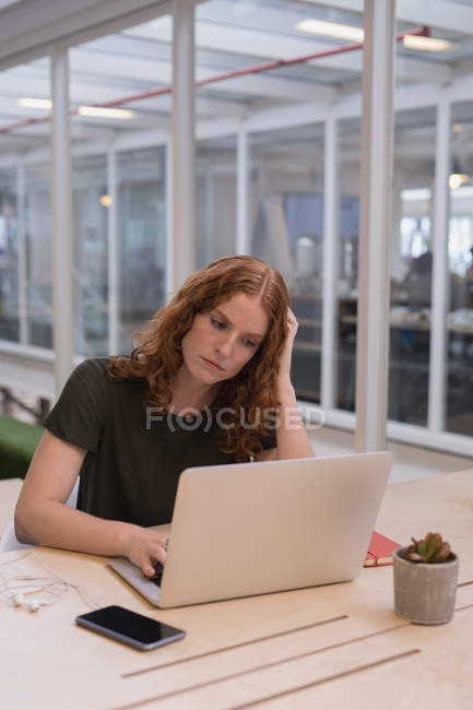 Female executive using laptop at desk in office — Stock Photo