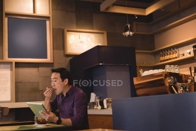 Asian man using digital tablet while eating in coffee shop — Stock Photo