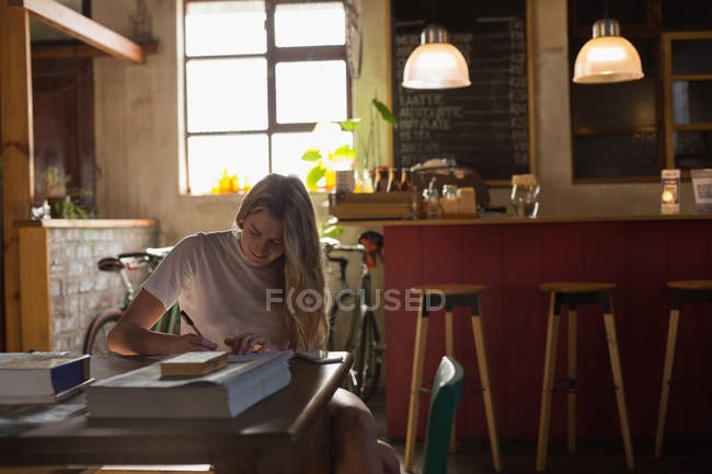 Giovane donna che scrive su un libro in un caffè — Foto stock
