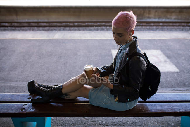 Young woman with pink hair listening music on mobile phone at railway station. — Stock Photo