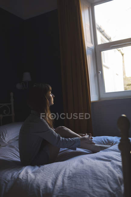 Donna che guarda la finestra mentre seduto sul letto a casa — Foto stock
