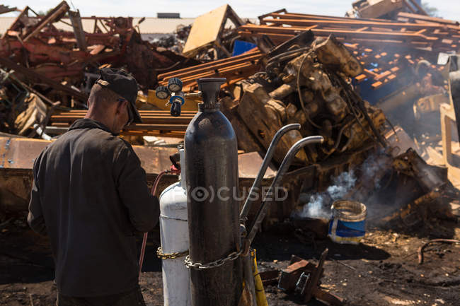 Trabajador de pie con una tubería cerca del cilindro en el desguace - foto de stock