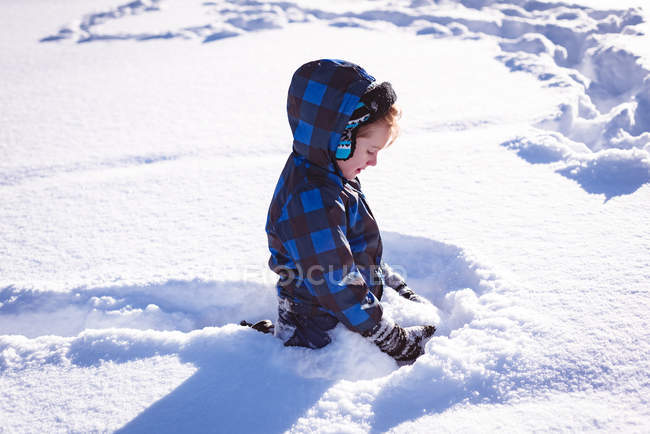 Rapaz bonito brincando na neve durante o inverno — Fotografia de Stock
