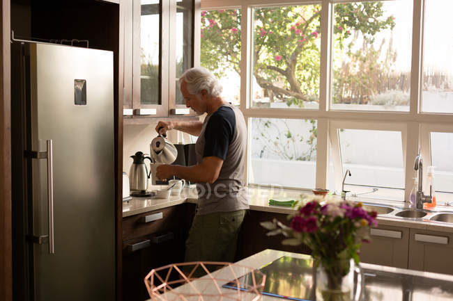 Старший мужчина наливает кофе на кухню дома — стоковое фото