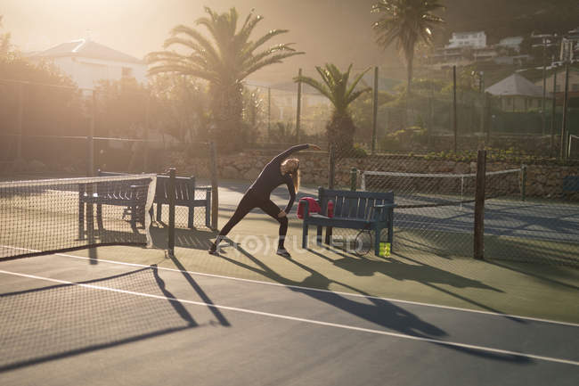 Женщина делает упражнения на растяжку на теннисном корте — стоковое фото