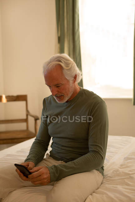 Uomo anziano che utilizza il telefono cellulare in camera da letto a casa — Foto stock