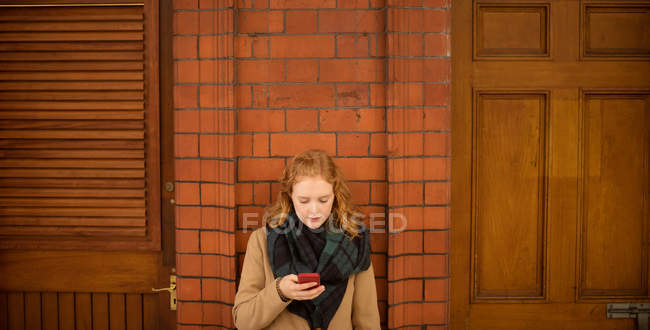 Young woman using mobile phone against wall — Stock Photo