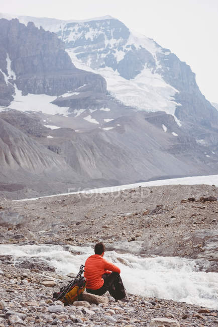 Senderista masculino con mochila relajante cerca del río - foto de stock