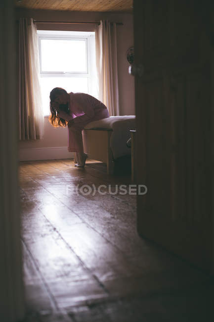 Femme tendue assise sur le lit dans la chambre à coucher à la maison — Photo de stock