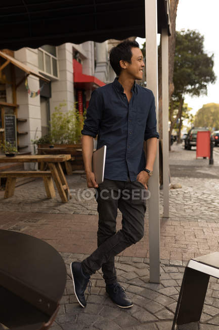 Smiling man in blue shirt with laptop standing in pavement cafe — Stock Photo