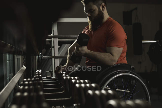 Deficiente homem em cadeira de rodas levantando halteres de rack no ginásio — Fotografia de Stock