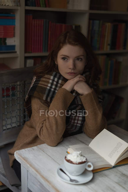 Mujer pensativa sentada en la sala de la biblioteca - foto de stock