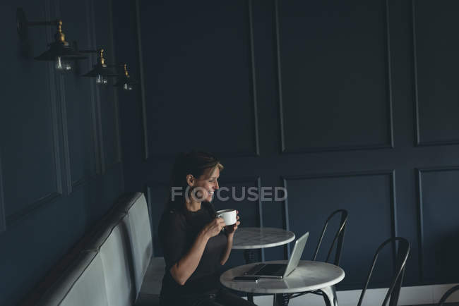 Donna d'affari che prende il caffè mentre usa il computer portatile in caffetteria a ufficio — Foto stock