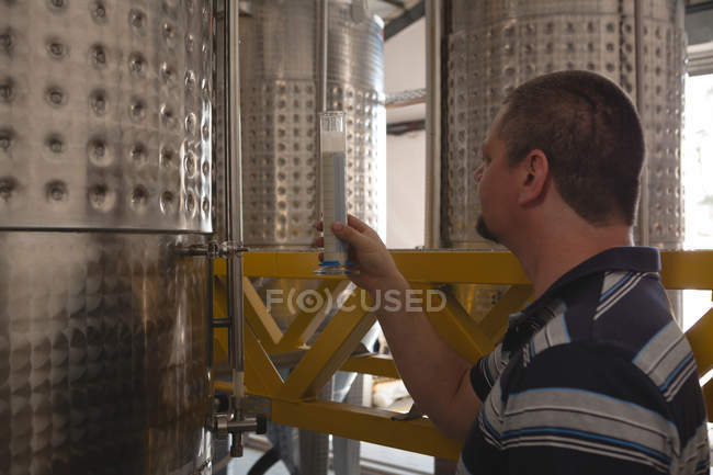 Рабочий мужчина осматривает джин в измерительном цилиндре на заводе — стоковое фото