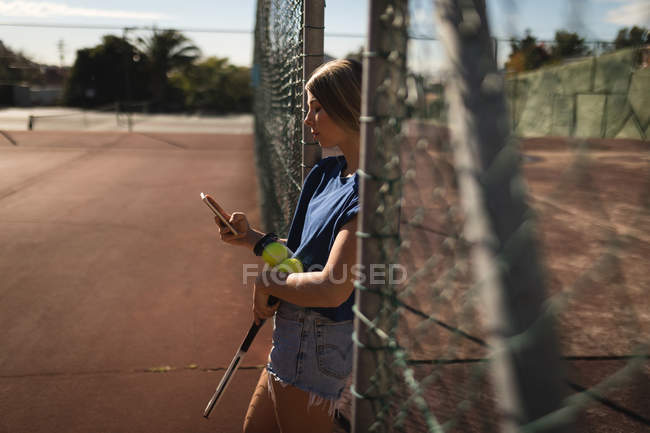 Молодая женщина с помощью мобильного телефона на теннисном корте — стоковое фото