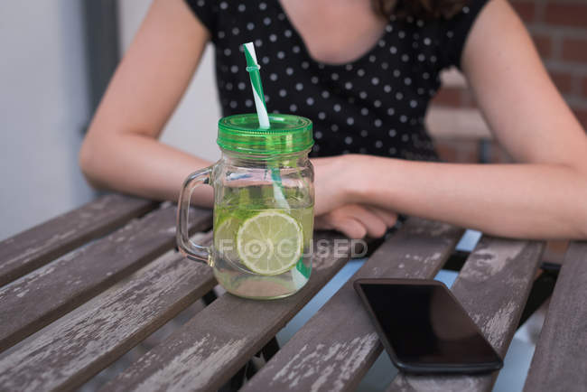 Крупный план лимонного сока и мобильного телефона на столе — стоковое фото
