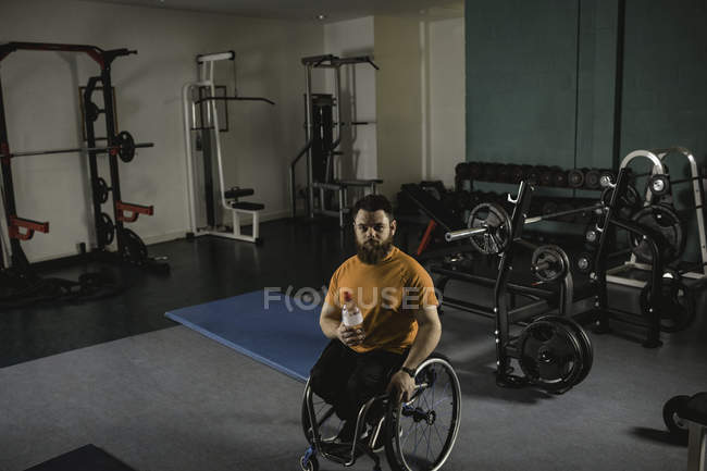 Jeune handicapé en fauteuil roulant avec bouteille d'eau dans la salle de gym — Photo de stock