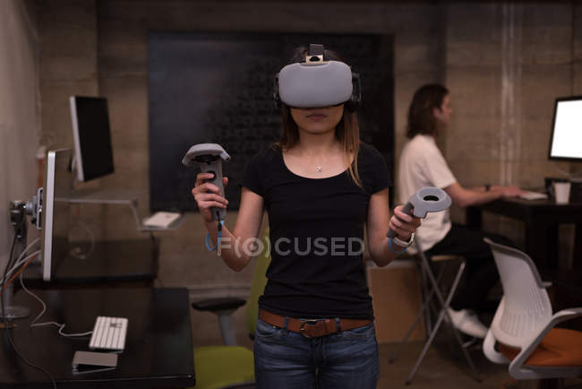 Ejecutiva femenina usando auriculares de realidad virtual con controlador en el interior de la oficina
. - foto de stock