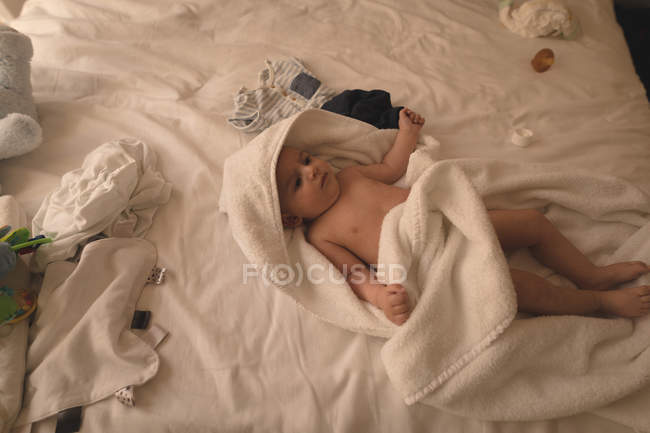 Cute baby lying on back in bathing towel on bed at home — Stock Photo