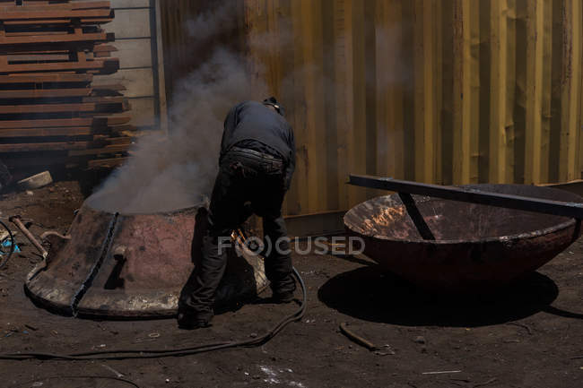 Trabalhador soldando a estrutura metálica enferrujada no scrapyard — Fotografia de Stock