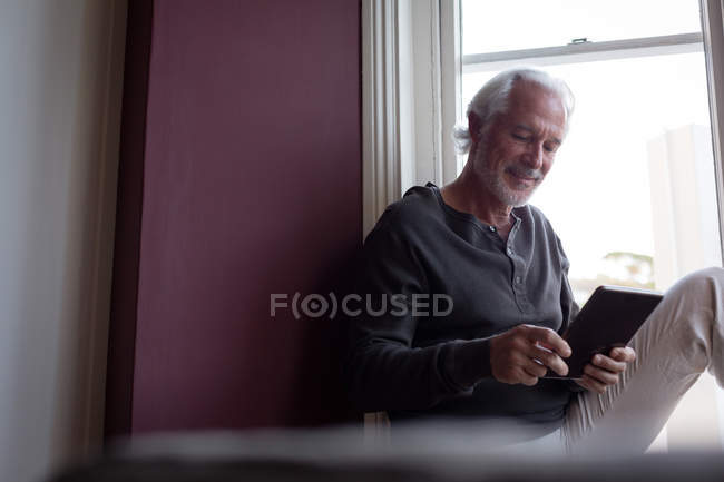 Старший чоловік, використовуючи цифровий планшетний біля вікна у вітальні на дому — стокове фото