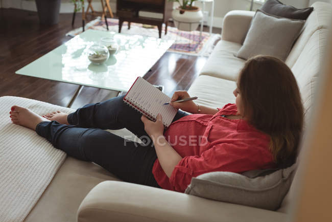 Femme enceinte écrivant dans un cahier à la maison — Photo de stock