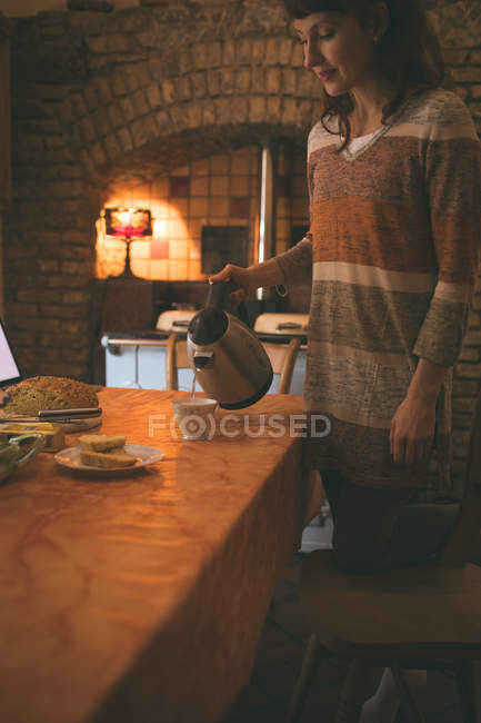 Bella donna versando acqua calda in tazza a casa — Foto stock