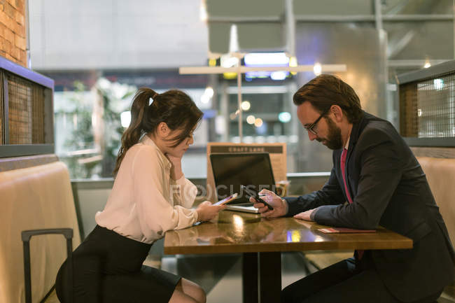 Empresario y mujer usando teléfono móvil en la sala de espera en el aeropuerto - foto de stock